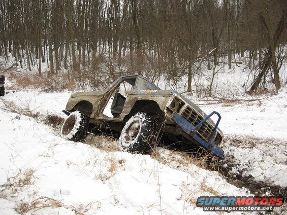 1979 Ford Bronco with doors removed, stuck in a snowy ditch with large off-road tires