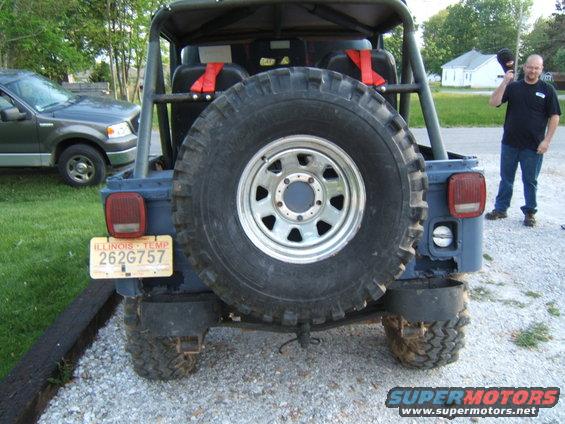 Dark blue Jeep CJ5 rear with spare tire, Illinois temp plate, and a man standing to the right