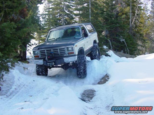 1986 Ford Bronco driving on a snowy trail with trees in the background