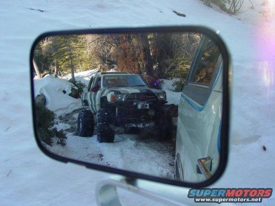 Modified pickup truck with large tires in snow, reflected in side mirror