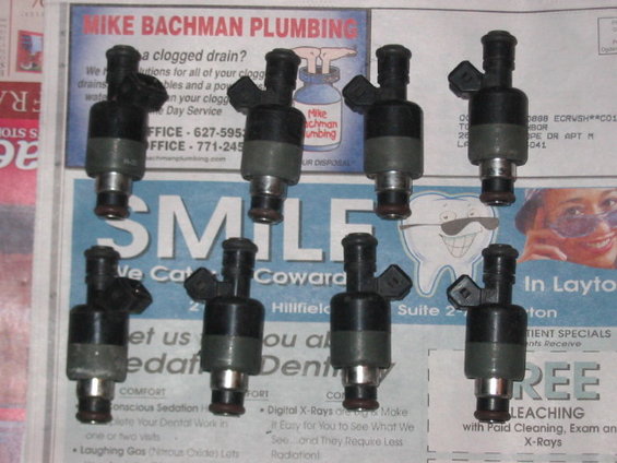Eight fuel injectors laid out on a newspaper