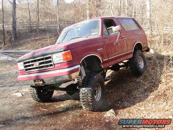 Red 1991 Ford Bronco with lifted suspension and large tires driving on a dirt hill
