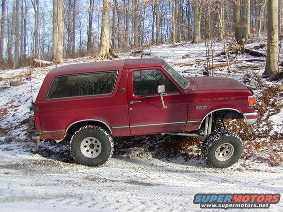 Red 1991 Ford Bronco with lifted suspension in snowy woods
