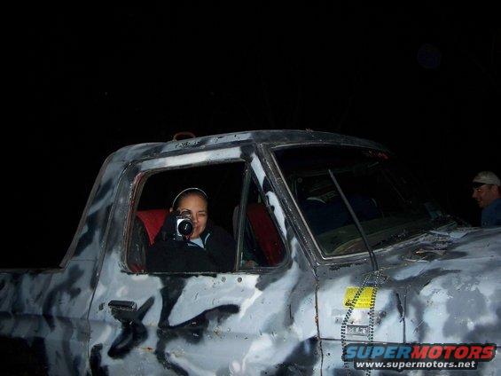 Woman in driver's seat of a camouflage-painted truck, holding a camera