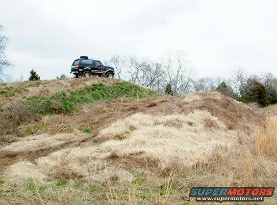 Black Ford Bronco parked on a grassy hill with trees in the background