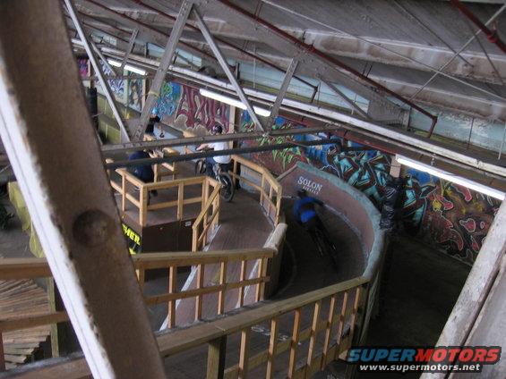 Indoor BMX track with wooden ramps and graffiti art on walls. People on bikes are visible