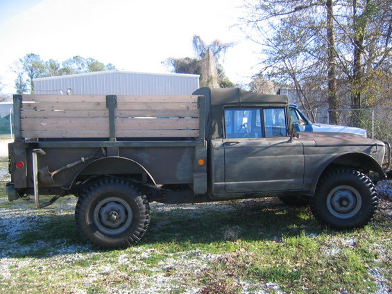 Side view of olive drab military truck with wooden bed and canvas top