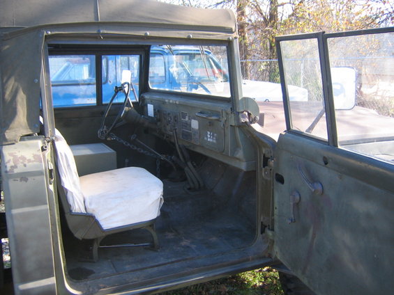 Green military truck interior with a white seat cover, exposed dashboard, and open door