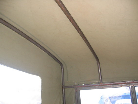 Inside a vehicle showing a canvas roof supported by metal bars. A window is visible on the left