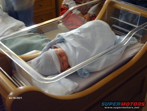 Newborn baby wrapped in blankets inside a hospital bassinet with a date stamp '04/10/2021'