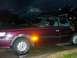 1991 Ford Bronco - A maroon sedan is parked outside at night, showing its side profile with an illuminated amber turn signal.