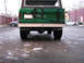 1975 Ford Bronco - The rear of a green SUV is shown, parked on a wet, debris-strewn surface with other vehicles nearby.