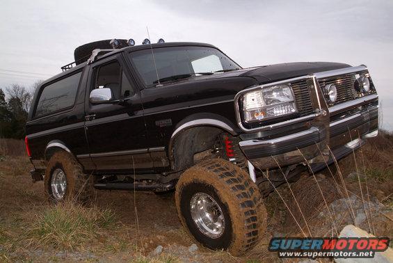Black Ford Bronco with off-road tires, roof rack, and light bar, angled on uneven terrain