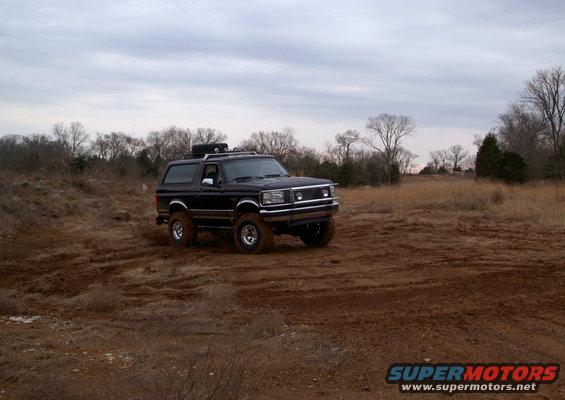 Black Ford Bronco with roof rack driving on a muddy field