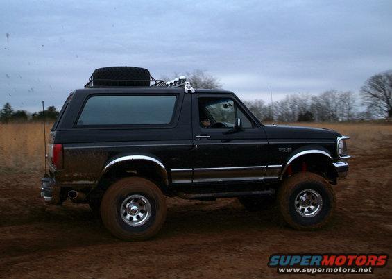 Black Ford Bronco with a spare tire on the roof rack, driving on a dirt road