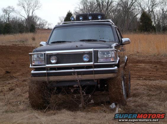 Black Ford Bronco with chrome grille guard, roof rack, and spare tire, stuck in mud