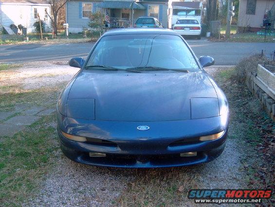 Blue Ford Probe parked in a driveway. It has pop-up headlights and a Ford logo on the front