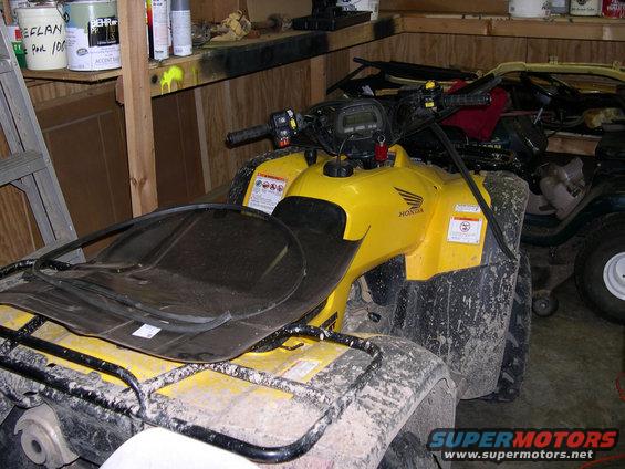 Yellow Honda ATV parked in a garage with another vehicle behind it