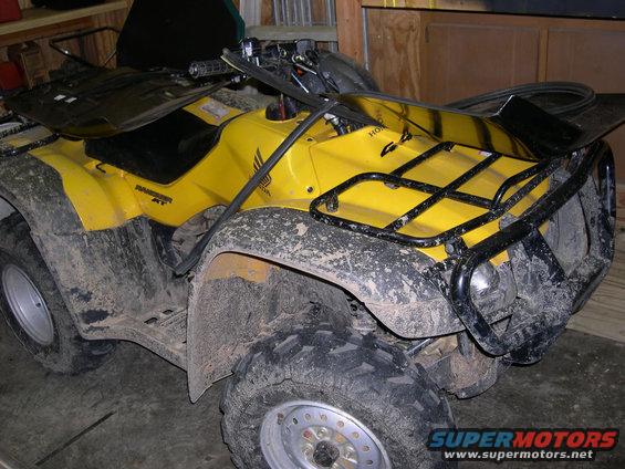Yellow Honda all-terrain vehicle with black racks, covered in mud