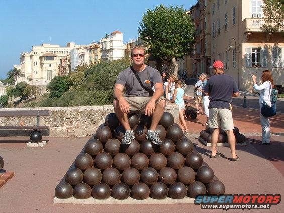 Man sits on cannonball pyramid in front of buildings