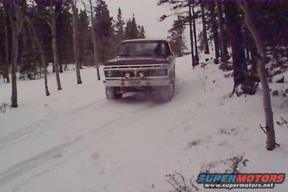 Brown 1978 Ford Bronco driving on a snowy road through a forest