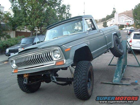 Green 1977 Jeep J-10 pickup truck with lifted suspension on an incline ramp