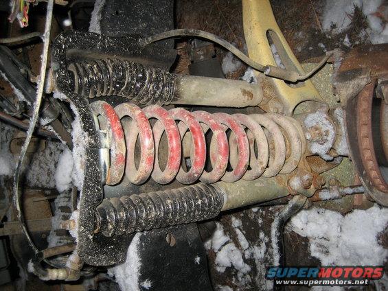 Front suspension part with red and black coil springs, covered in snow