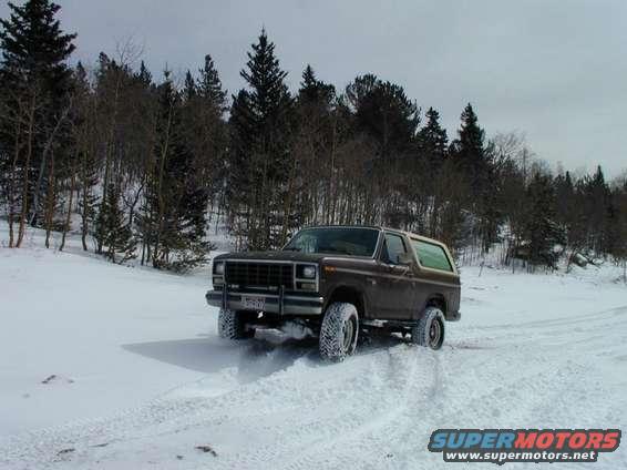 1980 Ford Bronco driving through snow with trees in background