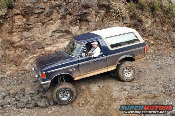 Blue and tan Ford Bronco off-roading on a rocky incline, driver visible
