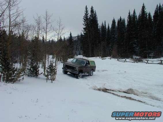 Brown 1980 Ford Bronco with a white top driving in snow, front-left quarter view