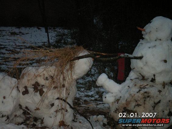 Two snowmen in a snowy yard, one with straw hair