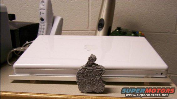 Gray statue in front of a white Apple laptop on a counter, with a cordless phone and other objects in the background