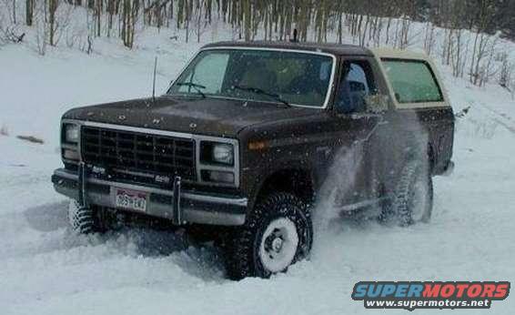 Brown 1980 Ford Bronco driving through snow, kicking up spray