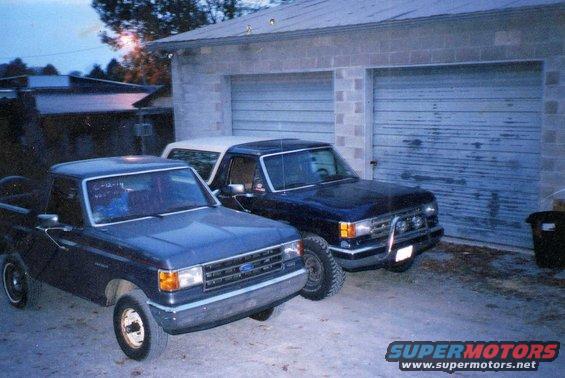 Dark blue Ford pickup truck and a dark blue Bronco parked in front of a garage