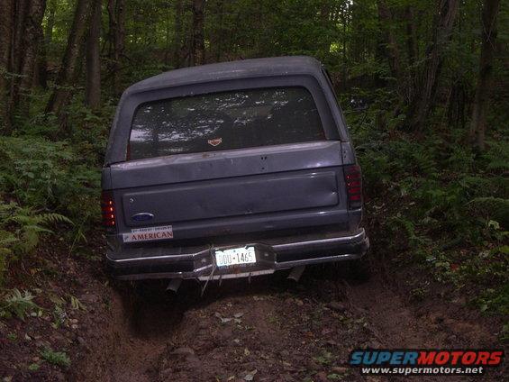 Gray Ford Bronco driving off-road on a muddy trail, rear view