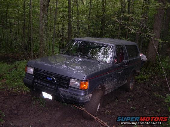 Gray Ford Bronco stuck in mud with a chain on the front tire