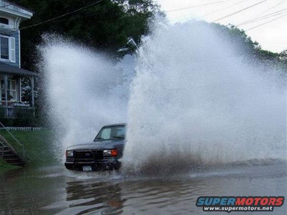 Dark colored truck driving through a flooded street, creating large splashes
