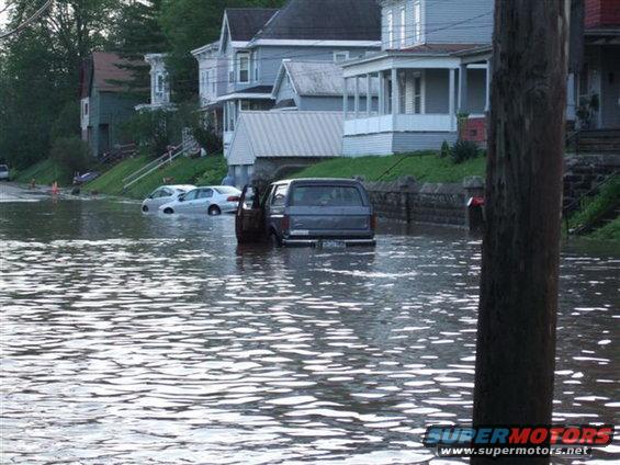 Dark SUV partially submerged in floodwater with other cars visible