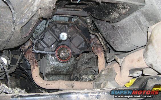 Underside view of a vehicle's engine and exhaust system, showing a transmission seal and rusty pipes