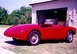 1959 MG A - A red 1959 MG A sports car is parked outside a garage, with a second vehicle visible within.