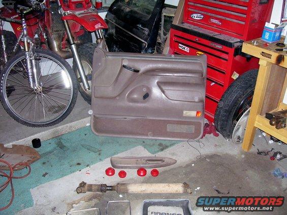 Brown Ford Bronco door panel with black handle and speaker grille, lying on a garage floor