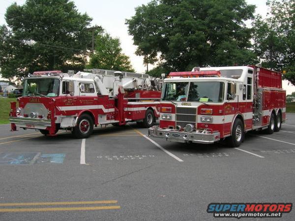 Two red and white fire trucks parked in a lot. One has a ladder