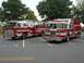 1989 Ford Bronco - Two fire trucks are parked in a lot, one equipped with a ladder, under a cloudy sky.