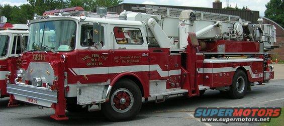 Red and white fire truck with ladder, marked "VOL. FIRE CO. NO. 1 GRILL, PA" and "TOWER 70". Another fire truck is partially visible to the left