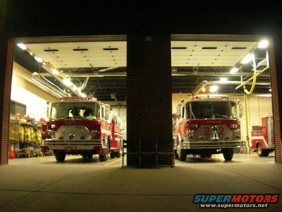 Two red fire trucks parked inside a fire station garage at night