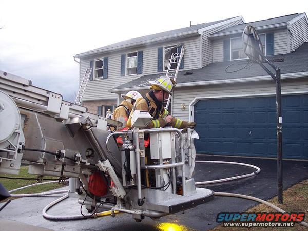 Firefighters on ladder truck with house in background