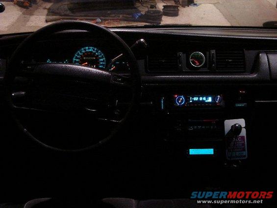 Car dashboard with glowing blue gauges and radio display. A small circular gauge is above the air vents