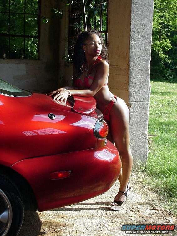 Woman in red bikini leaning on the rear quarter panel of a red sports car