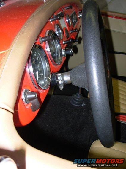 Dashboard with gauges and black steering wheel. Red dash panel has switches and knobs. Tan interior trim visible