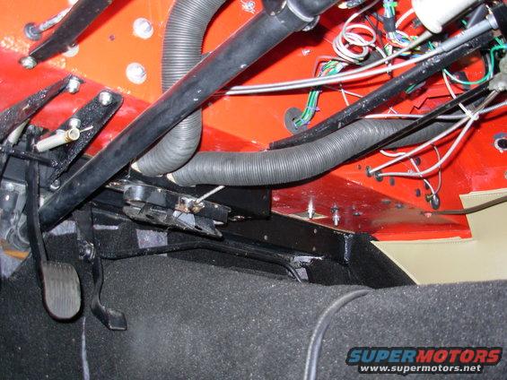 Car interior showing brake and clutch pedals, black carpeting, and exposed wiring with red firewall